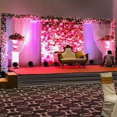 a stage set up for a wedding with flowers on the wall and couches in front