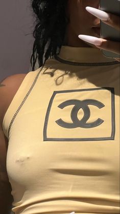 a woman holding a cell phone in her right hand and wearing a yellow tank top with a chanel logo on it