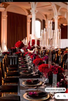 a long table is set with black and gold place settings, red flower centerpieces, and silverware