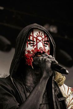 a man with painted face and hood holding a microphone in his hand while standing on stage