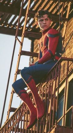 a man in spider - man suit sitting on top of a metal staircase next to a brick building