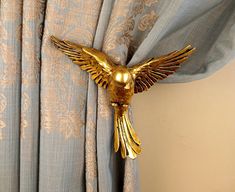 a gold bird is hanging on the curtain in front of a blue drapeside