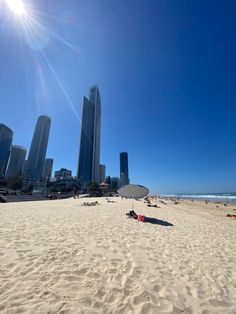 the sun shines brightly over a beach with people relaxing on it and skyscrapers in the background