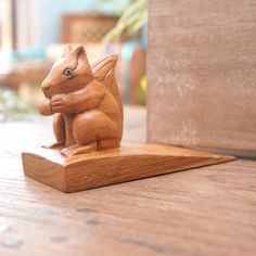 a small wooden squirrel figurine sitting on top of a wooden table next to a potted plant