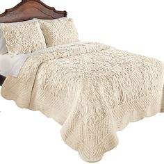 a bed with a white comforter on top of it next to a wooden headboard