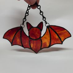 a stained glass bat hanging from a chain on a white background with a person's hand holding it