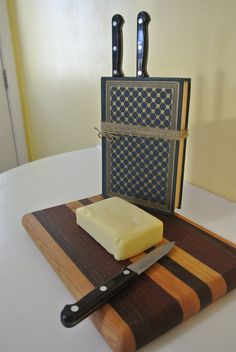 a cutting board with a knife and block of butter on it next to a pair of knives