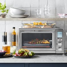 a silver toaster oven sitting on top of a counter next to plates and bowls