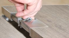 a hand that is touching the edge of a piece of metal on a wooden table