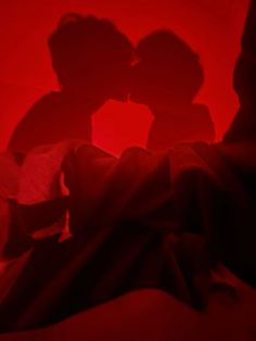 the shadow of two people kissing in front of a red background