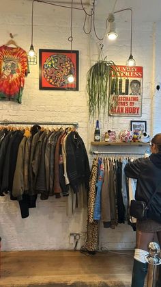 a woman standing in front of a rack of shirts and pants hanging on the wall