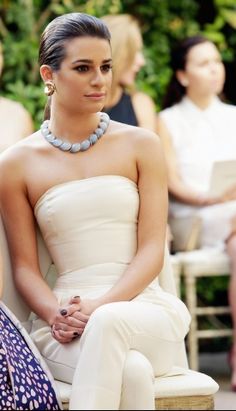 a woman sitting on top of a white chair next to another woman in a dress