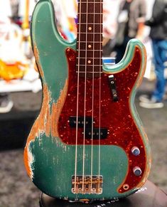 an old green and red guitar sitting on top of a black stand with people in the background