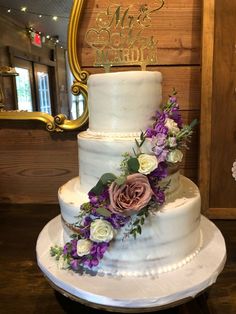 a three tiered cake with flowers on the side and a mirror in the background