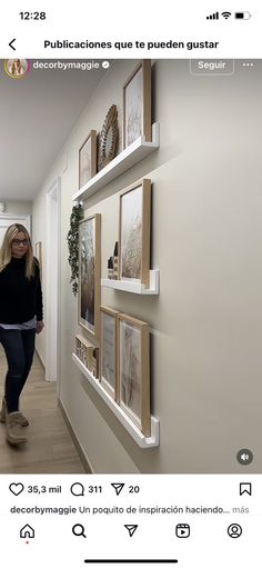 a woman walking down a hallway next to a wall with pictures hanging on the walls