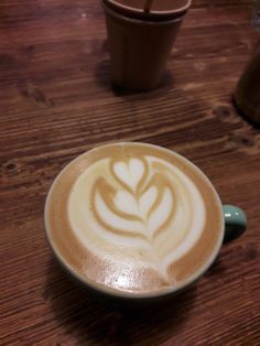 a cappuccino on a wooden table with two cups in the background