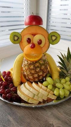 a plate with fruit and a monkey made out of bananas, grapes, apples, and pineapples