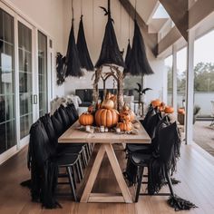 a wooden table topped with lots of pumpkins next to black chairs and umbrellas