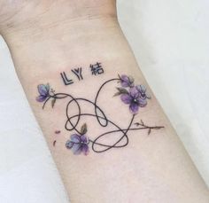 a small wrist tattoo with purple flowers and the word ly written in cursive writing