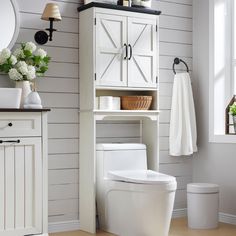 a white toilet sitting in a bathroom next to a cabinet and sink with flowers on it