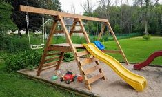 a wooden swing set with a slide in the sand and some toys on the ground