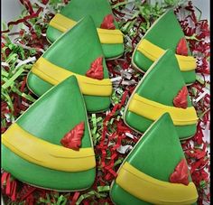 green and yellow decorated cookies with red bows on them in a box filled with tinsel