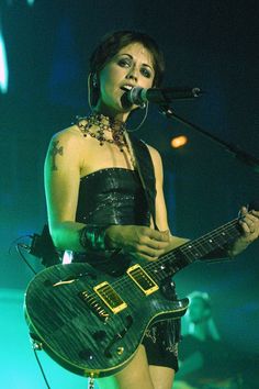 a woman holding a guitar while standing in front of a microphone