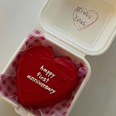 a red heart shaped cake in a plastic container with writing on it and the words happy first anniversary