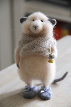 a needle - felted mouse is standing on its hind legs and holding a bell