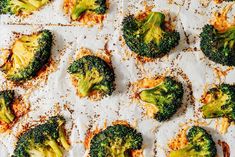 broccoli florets are arranged on a sheet of parchment paper with seasoning sprinkles