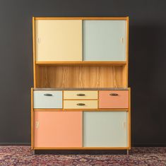 an old fashioned cabinet with drawers and cupboards on it's sides, in front of a gray wall