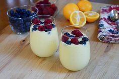 two glasses filled with yogurt, berries and blueberries on a cutting board