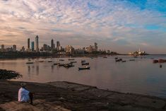 a man sitting on the edge of a river watching boats in the water