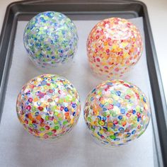 three glass balls are on a tray with confetti sprinkles all over them