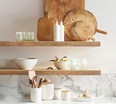 two wooden shelves with bowls and utensils on them in a white marble kitchen