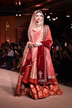 a woman in a red and gold bridal gown on the catwalk at a fashion show