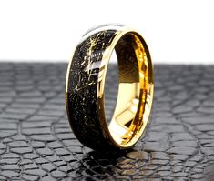 a wedding ring with black and gold inlays on the outside, sitting on a shiny surface