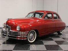 an old red car is parked on a black and white checkered floor