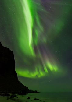 an aurora bore in the night sky with green and purple lights above it, over a rocky