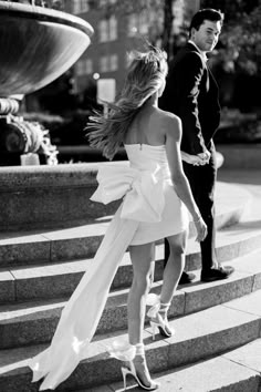 a woman in a white dress walking down some steps with a man standing behind her