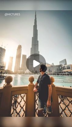 a man standing on top of a bridge next to a body of water with tall buildings in the background