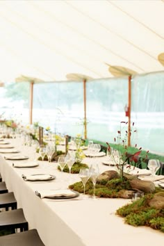 a long table is set with white plates and place settings for an outdoor dinner party