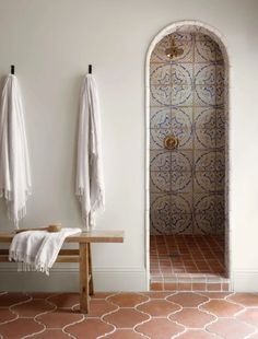 two white towels hanging on the wall next to a wooden table and bench in a bathroom