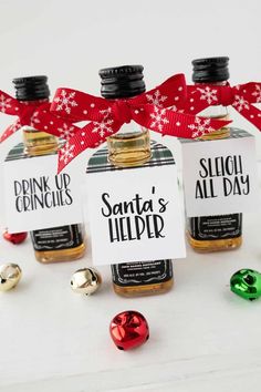 three bottles of santa's helper with christmas decorations around them on a white surface