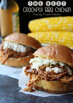 two pulled pork sandwiches with cole slaw on the side and corn on the cob in the background