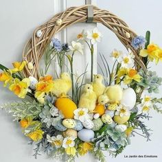 an easter wreath with yellow and white flowers, eggs and chicks on it is hanging from the front door