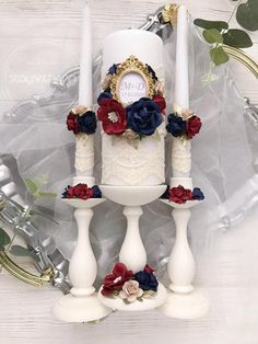 a wedding cake decorated with red, white and blue flowers sits on top of two candles