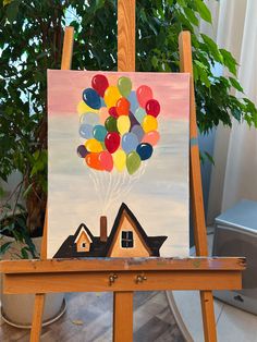 an easel with a painting on it that has balloons in the sky and a house