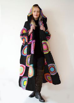 a woman standing in front of a white wall wearing a black coat with multicolored circles on it