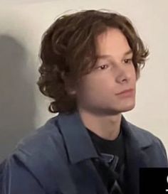 a young man with curly hair wearing a blue shirt and black tie looking off to the side